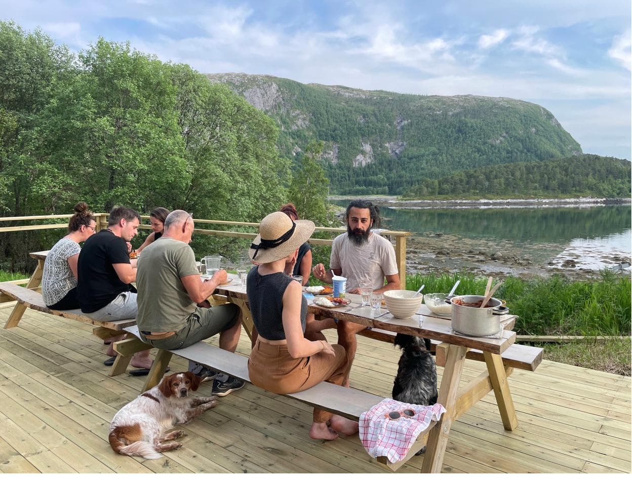 Group of people dining at outdoor table by the fjord